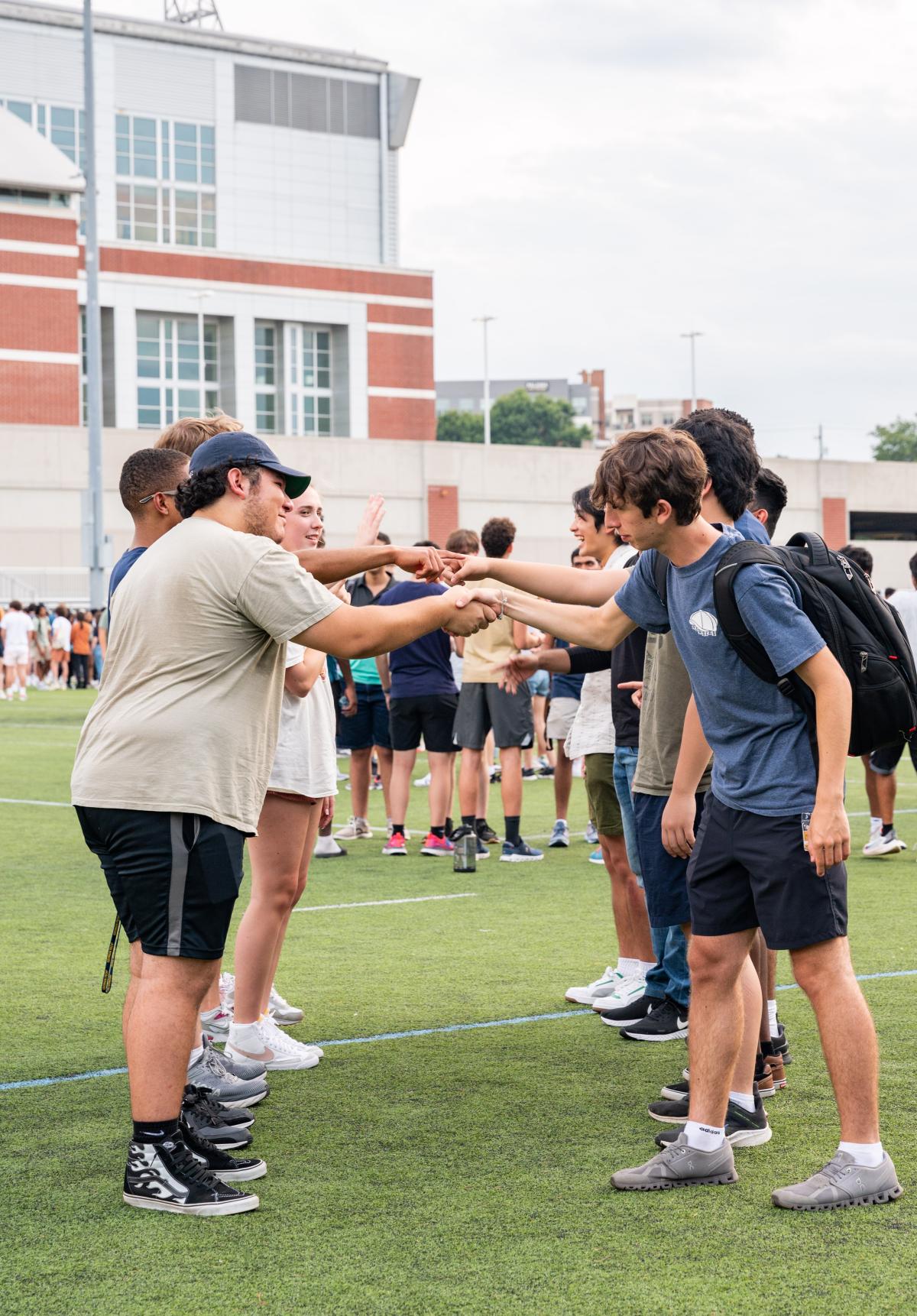 Four students fistbumping each other while standing on a green field